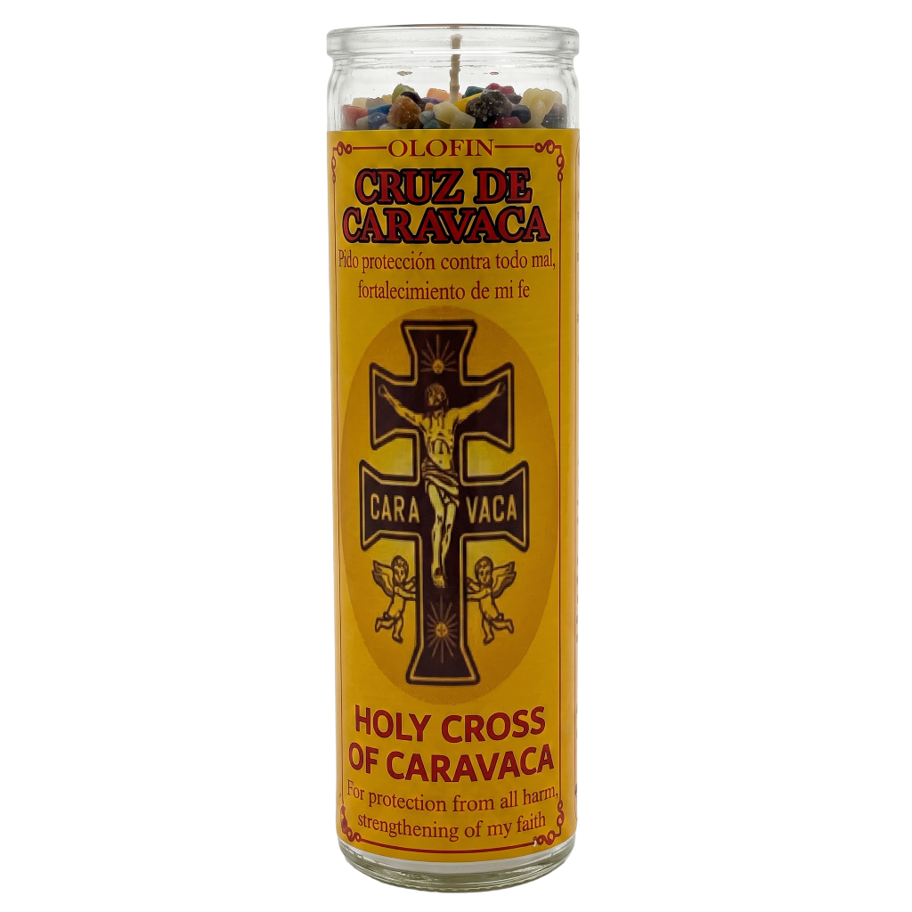 A tall glass jar candle with a yellow label reading 'Cruz de Caravaca' and 'Holy Cross of Caravaca,' featuring a black crucifix graphic and multicolored wax pieces visible at the top.