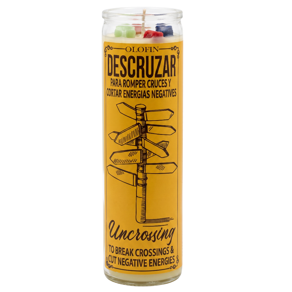 A tall glass jar candle with a yellow label reading 'OLOFIN DESCRUZAR' and 'UNCROSSING', featuring a black directional sign illustration and multicolored wax pieces visible at the top.