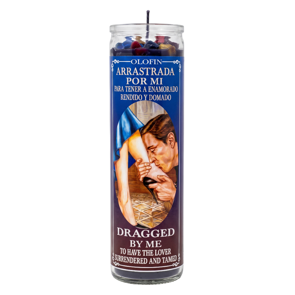 A tall glass prayer candle with a dark blue label reading 'Olofin Arrastrada Por Mi' and 'Dragged By Me To Have The Lover Rendered And Tamed,' featuring an illustration of a man holding a woman's leg.