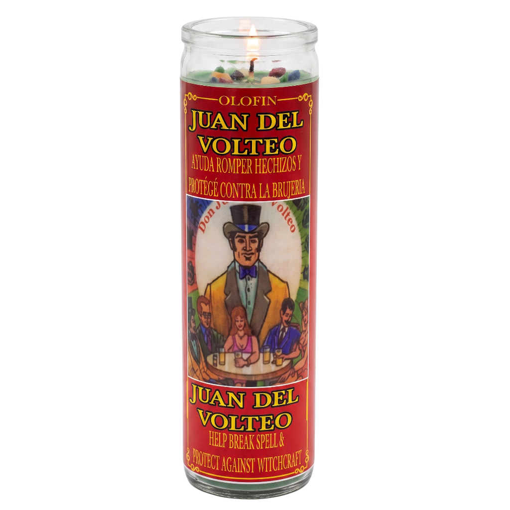A tall glass jar candle labeled 'Juan del Volteo' with a red label and printed illustration, shown lit on a plain white background.