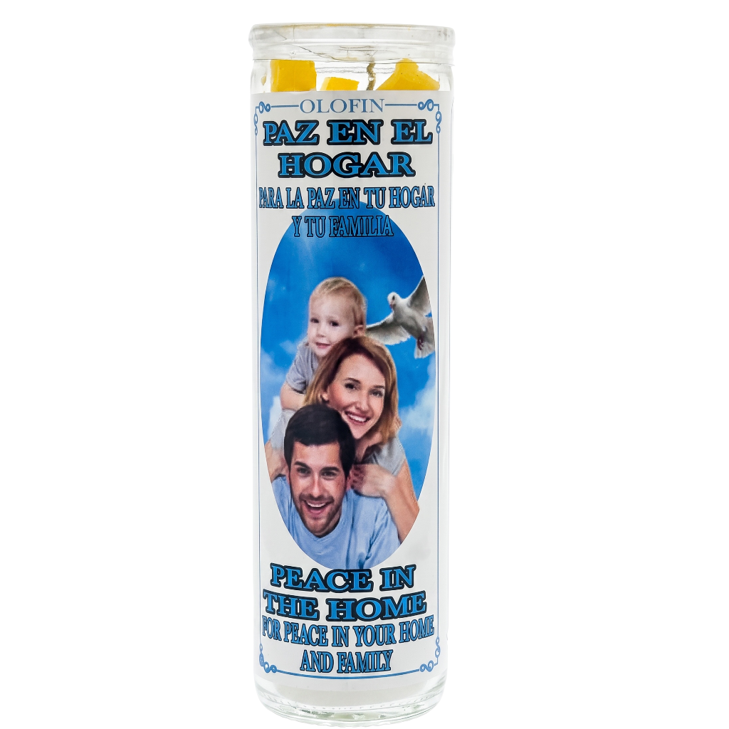 A personalized glass prayer candle featuring a printed family photo and Spanish and English text that reads 'Peace in the Home' and 'For Peace in Your Home and Family.' The candle has a clear glass body with yellow wax at the top and blue printed graphics.
