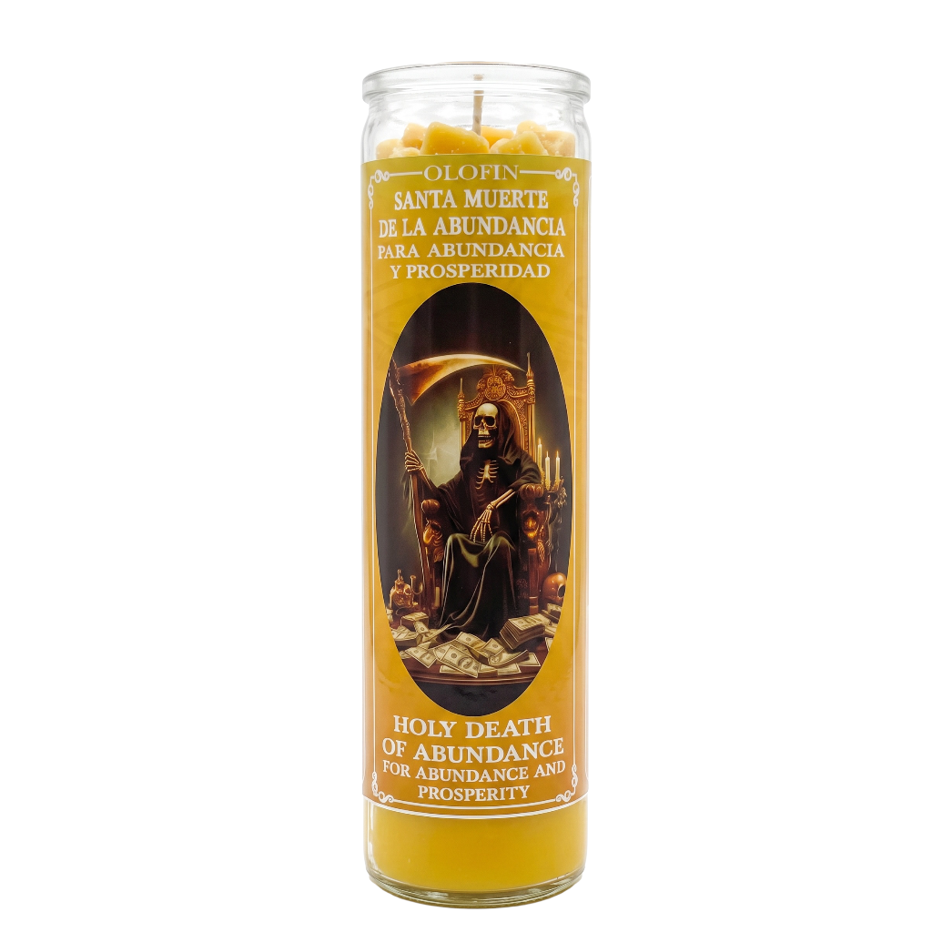 A tall glass jar candle with a yellow wax body and a printed label featuring Santa Muerte. The label includes Spanish text ('Santa Muerte de la abundancia para abundancia y prosperidad') and English text ('Holy Death of Abundance for Abundance and Prosperity').