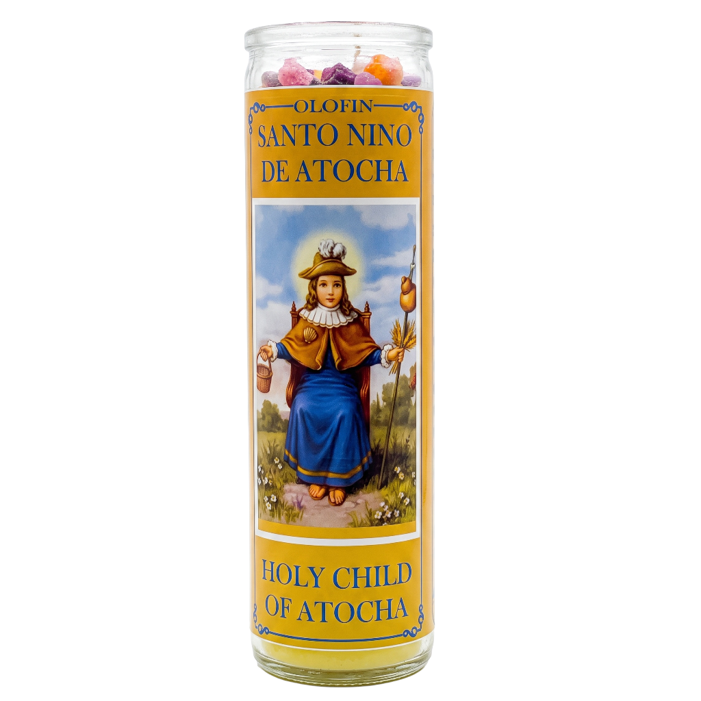A tall glass jar candle labeled 'Olofin Santo Nino de Atocha' and 'Holy Child of Atocha,' featuring a printed illustration of a child in a blue dress on a yellow label, shown on a white background.